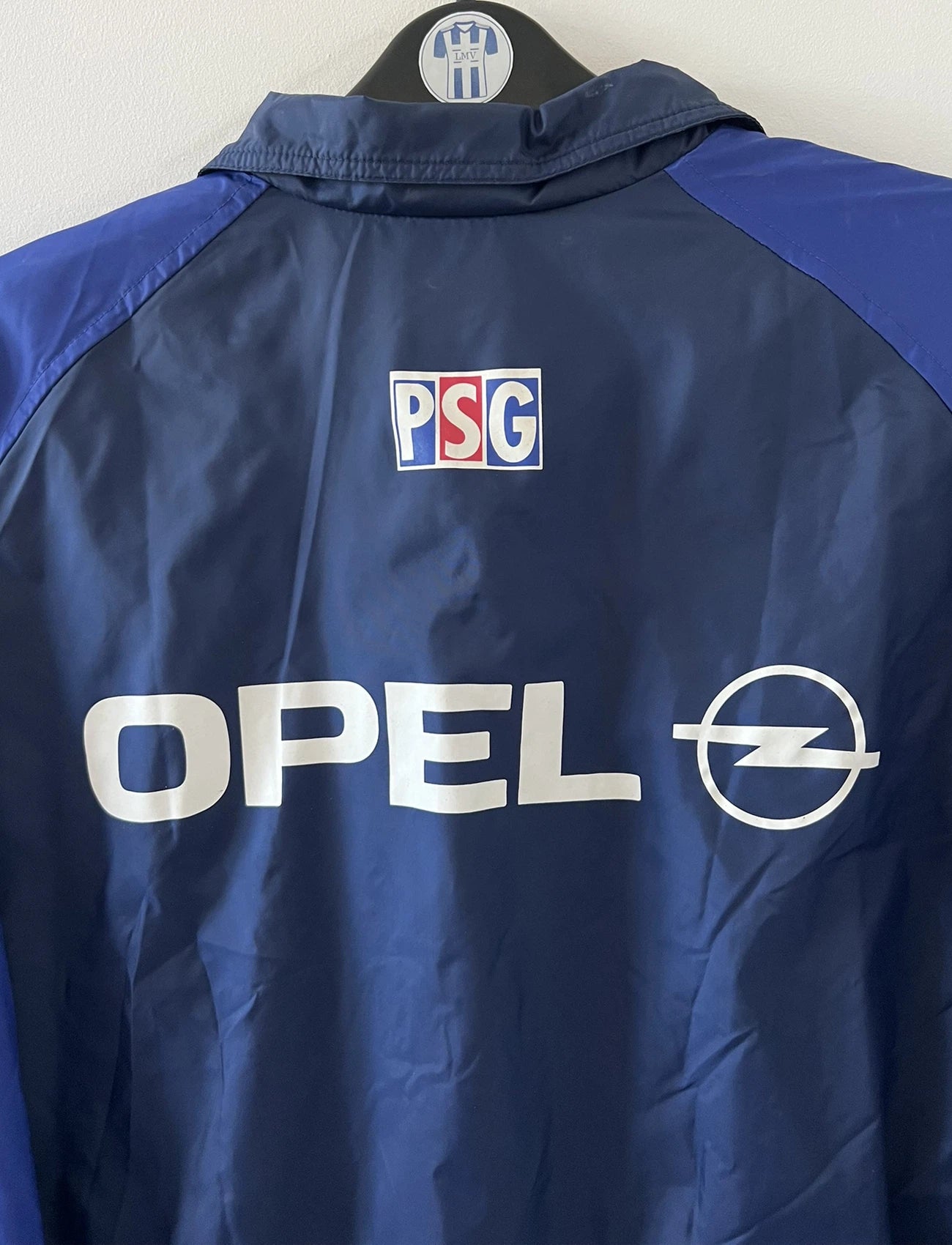 Veste bleue du PSG de la saison 1998/1999. On peut retrouver l'équipementier Nike et le sponsor Opel. Il s'agit d'une veste authentique d'époque.