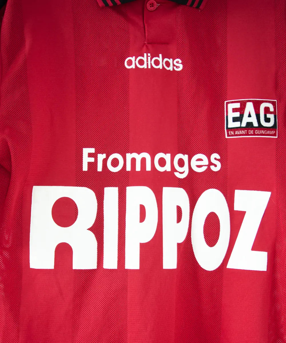 Maillot domicile rouge et noir de l'EA Guingamp de la saison 1996/1997. On peut retrouver le sponsor fromage rippoz et l'équipementier adidas