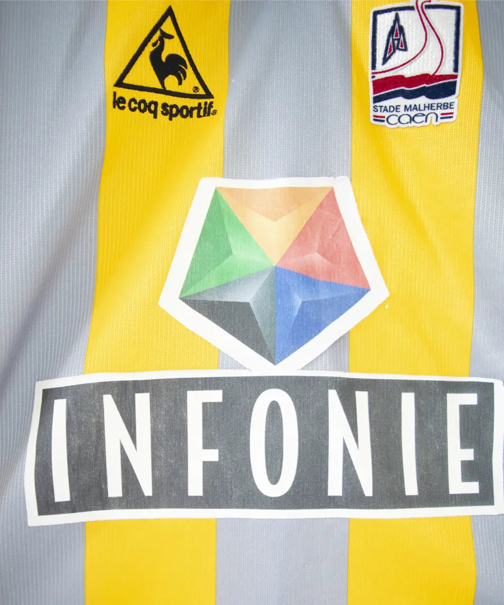 Maillot du SM Caen de la saison 2000-2001. Le maillot est de couleur gris et jaune. On peut retrouver l'équipementier le coq sportif, le sponsor infonie et le sponsor isigny sainte mère. On peut aussi retrouver l'ancien patch LNF. Le maillot est floqué du numéro 20 Faderne