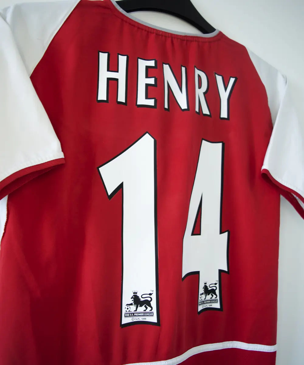 maillot authentique arsenal 2002-2004. Le maillot est de couleur rouge et blanche. On peut retrouver le sponsor O2 en feutrine et l'équipementier nike. Le maillot est floqué du numéro 14 Thierry Henry. Sur cette photo on peut voir le flocage de côté