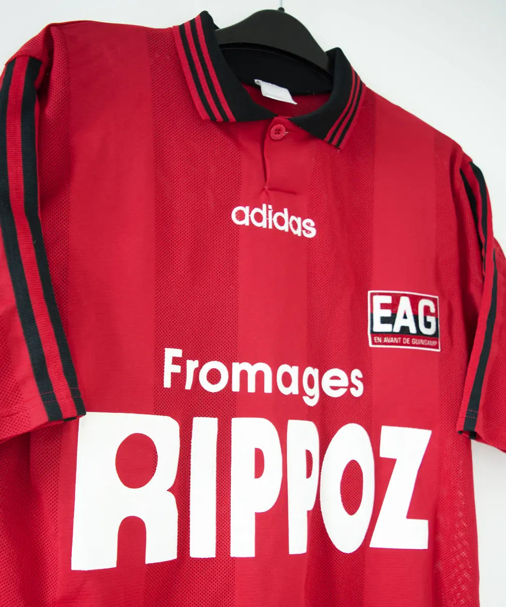 Maillot domicile rouge et noir de l'EA Guingamp de la saison 1996/1997. On peut retrouver le sponsor fromage rippoz et l'équipementier adidas