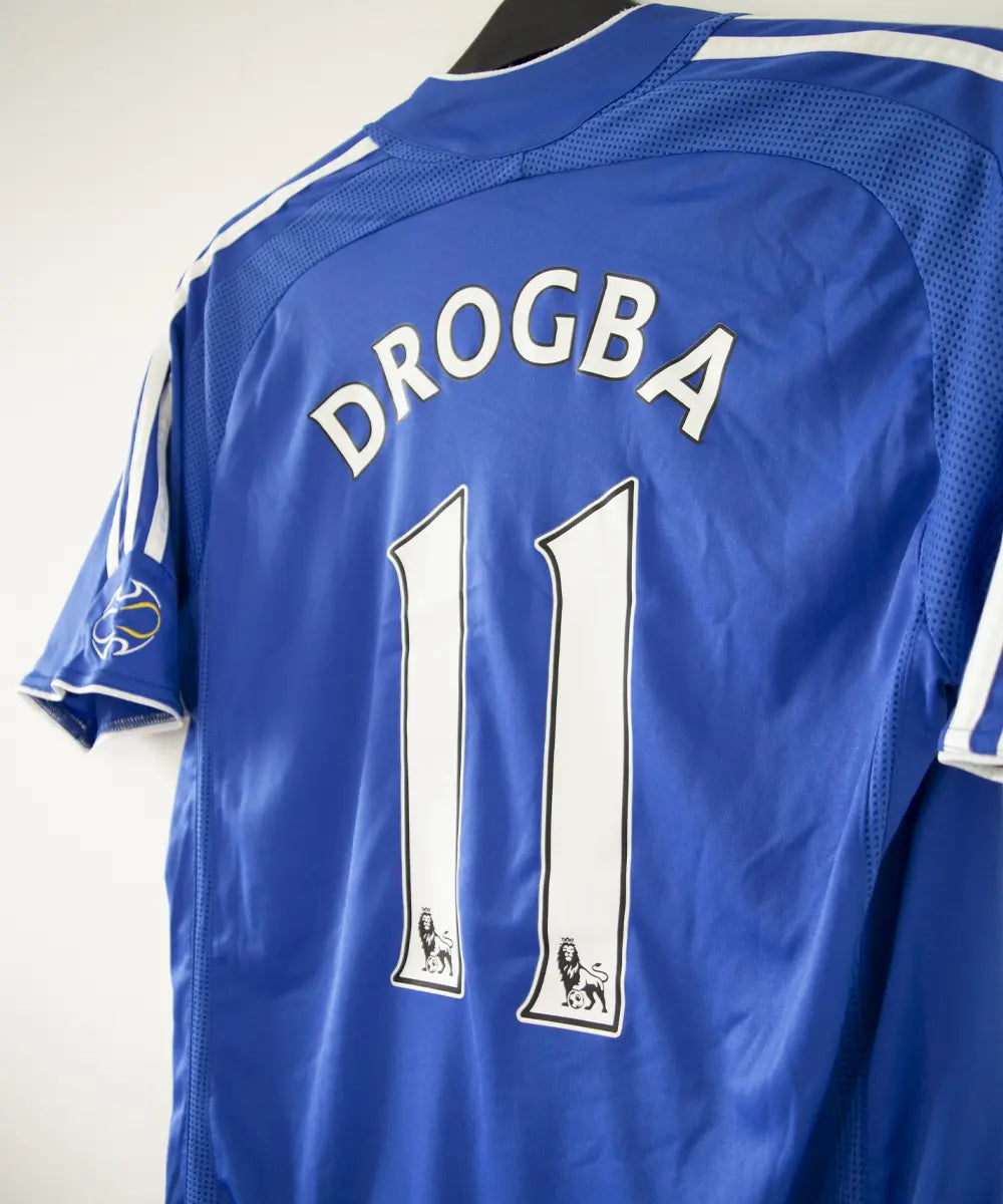Maillot de foot vintage bleu domicile de chelsea de la saison 2006-2008. On peut retrouver l'équipementier adidas et le sponsor samsung. Le maillot est floqué du numéro 11 Didier Drogba. Le maillot possède l'étiquette 061230