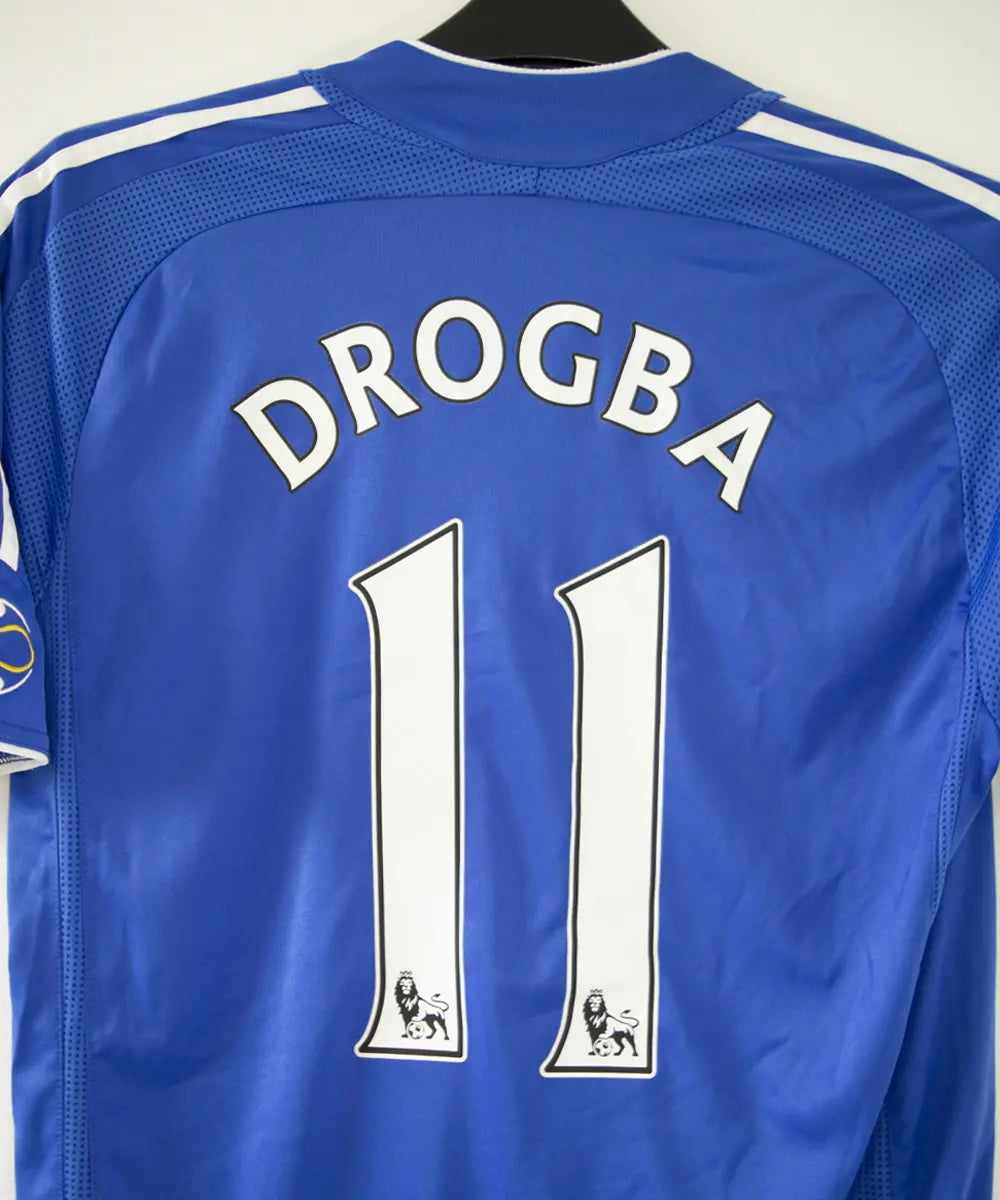 Maillot de foot vintage bleu domicile de chelsea de la saison 2006-2008. On peut retrouver l'équipementier adidas et le sponsor samsung. Le maillot est floqué du numéro 11 Didier Drogba. Le maillot possède l'étiquette 061230
