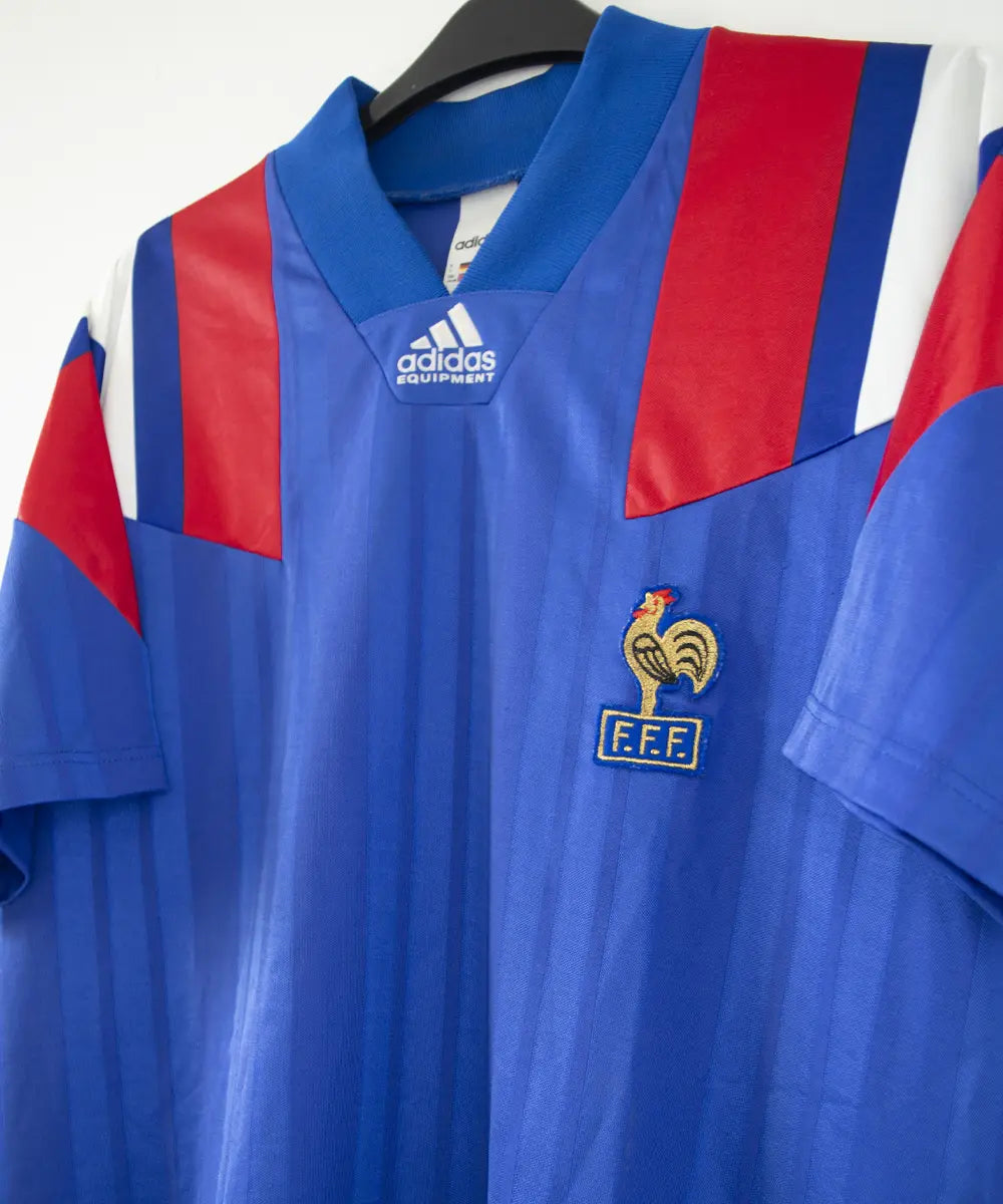 Maillot domicile de l'équipe de france 1992 de couleur bleu blanc et rouge. On peut retrouver l'équipementier adidas