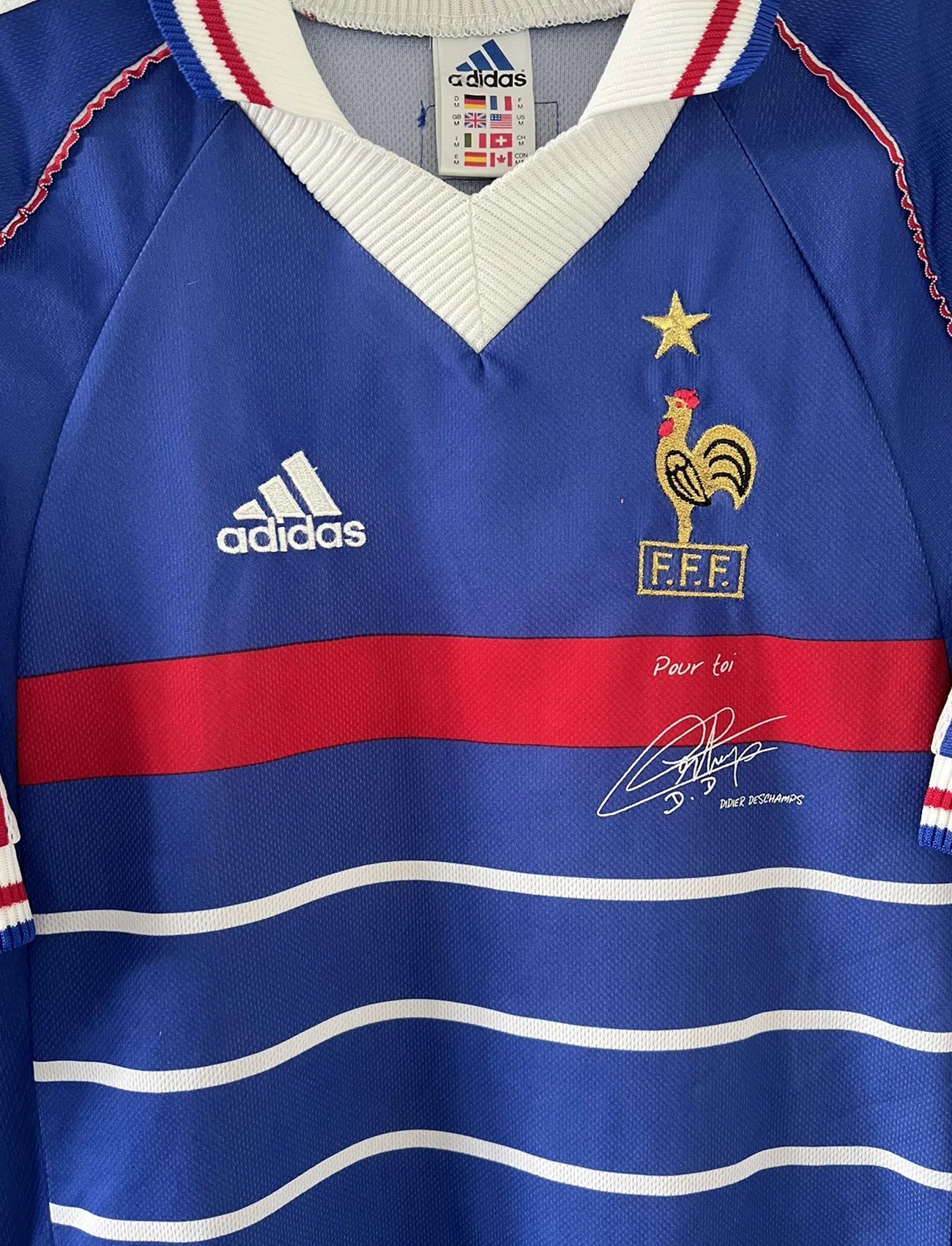 Maillot de foot vintage de l'équipe de france bleu blanc et rouge. Il s'agit du maillot domicile de la coupe du monde 1998. On peut retrouver l'équipementier adidas et le coq avec l'étoile. Le maillot possède la signature pour toi de Didier Deschamps