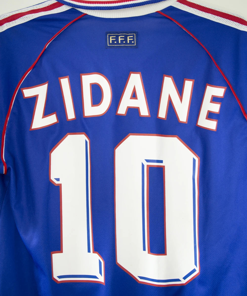 Maillot vintage domicile bleu, blanc et rouge de l'équipe de france 1998. On peut retrouver l'équipementier adidas. Le maillot est floqué du numéro 10 Zinedine Zidane avec le flocage à l'avant et à l'arrière du maillot. Il s'agit d'un maillot authentique d'époque
