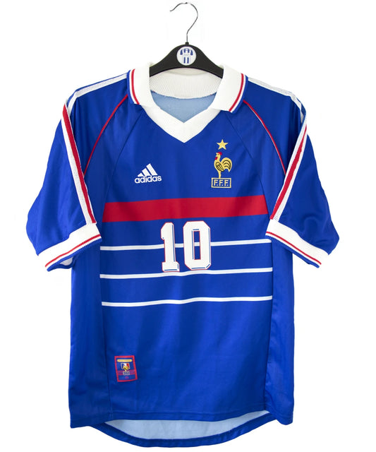 Maillot vintage domicile bleu, blanc et rouge de l'équipe de france 1998. On peut retrouver l'équipementier adidas. Le maillot est floqué du numéro 10 Zinedine Zidane avec le flocage à l'avant et à l'arrière du maillot. Il s'agit d'un maillot authentique d'époque