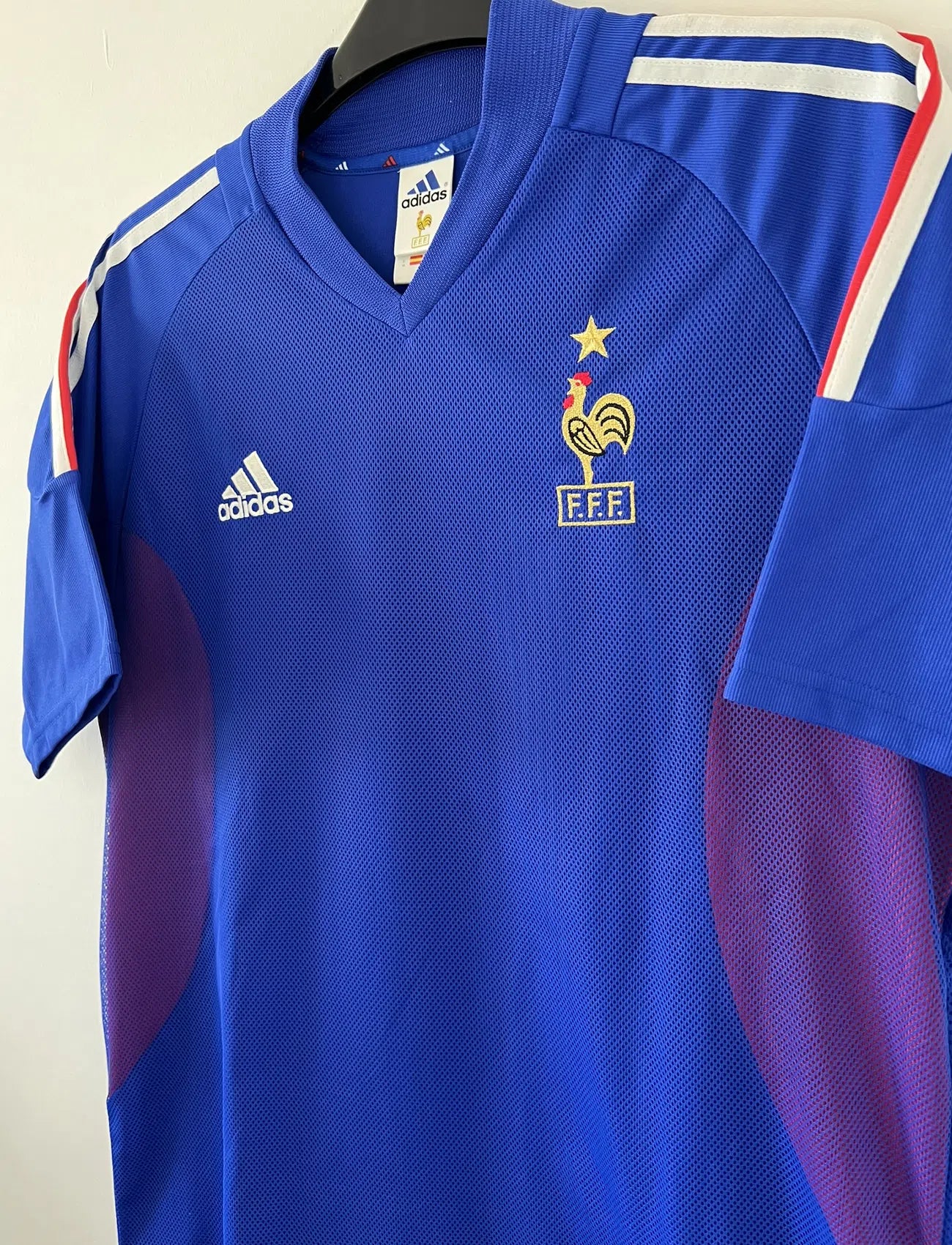 Maillot de foot vintage domicile de l'Equipe de France 2002. Le maillot est de couleur bleu, blanc et rouge. On peut retrouver l'équipementier adidas et le flocage de Zinedine Zidane. Il s'agit d'un maillot authentique. Le maillot possède l'étiquette d'authenticité comportant les numéros 139531.