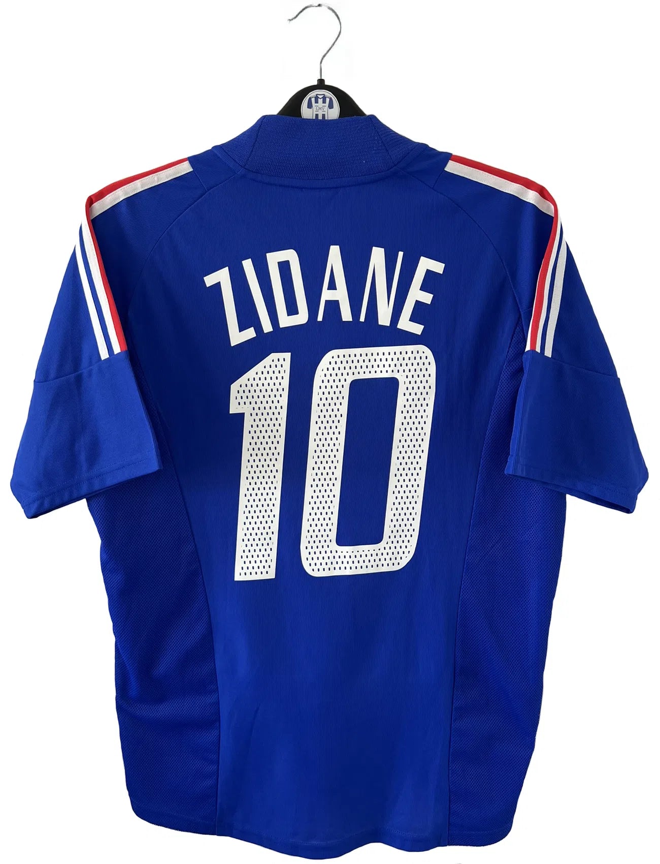 Maillot de foot vintage domicile de l'Equipe de France 2002. Le maillot est de couleur bleu, blanc et rouge. On peut retrouver l'équipementier adidas et le flocage de Zinedine Zidane. Il s'agit d'un maillot authentique. Le maillot possède l'étiquette d'authenticité comportant les numéros 139531.