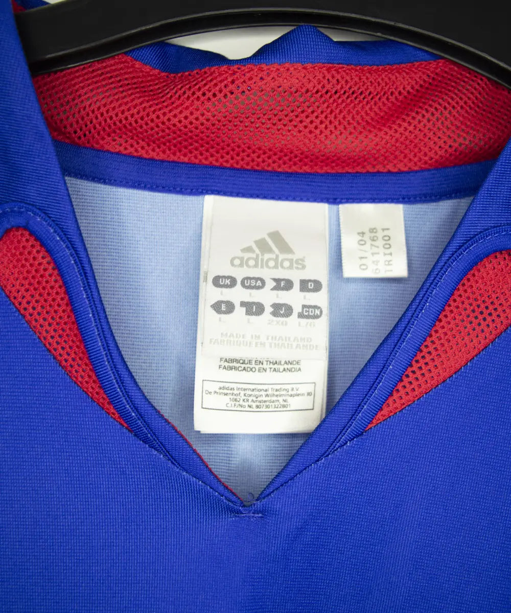 Maillot domicile bleu, blanc et rouge de l'équipe de france 2004-2006. On peut retrouver l'équipementier adidas. Le maillot est floqué du numéro 12 Thierry Henry. Sur cette photo on peut voir l'étiquette d'authenticité comportant les numéros 641768