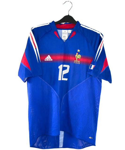 Maillot domicile bleu, blanc et rouge de l'équipe de france 2004-2006. On peut retrouver l'équipementier adidas. Le maillot est floqué du numéro 12 Thierry Henry