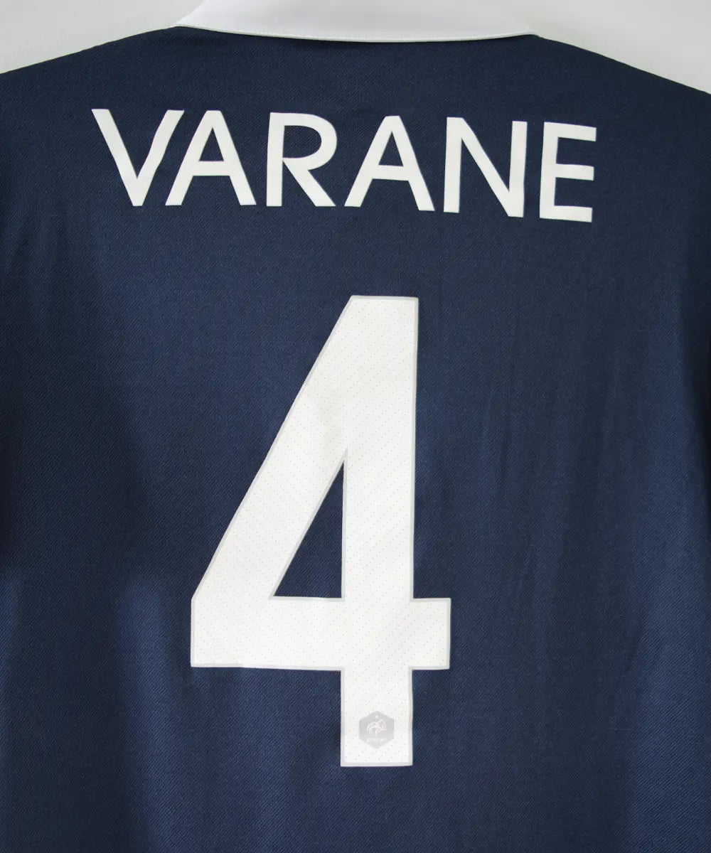 Maillot domicile équipe de france édité lors de la coupe du monde 2014. Le maillot est de couleur bleu et blanc. On peut retrouver l'équipementier nike. Le maillot est floqué du numéro 4 Varane. Sur cette photo on peut voir le flocage de près