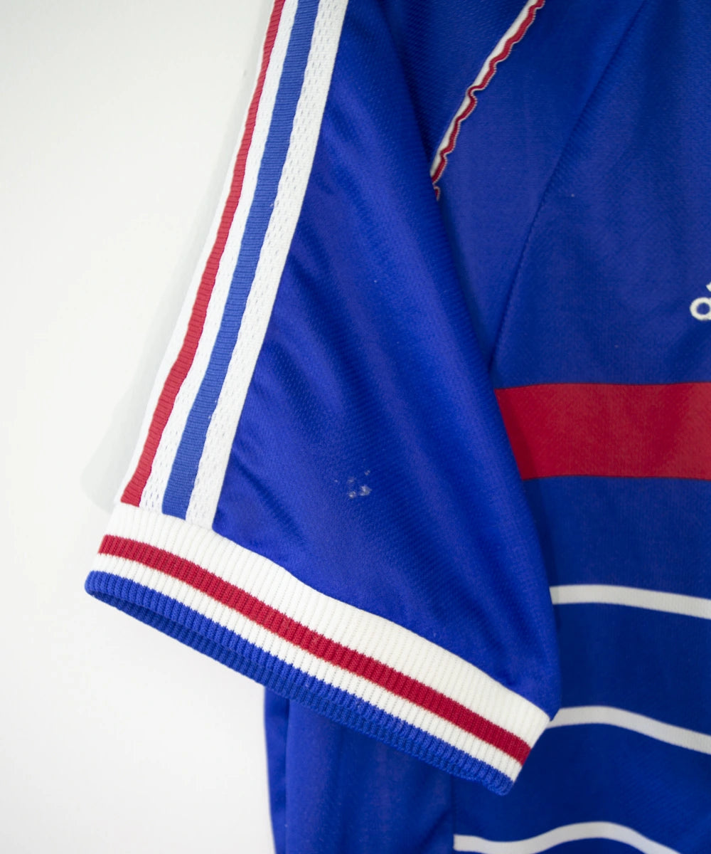 Maillot de foot vintage bleu, blanc et rouge de l'équipe de france 1998. On peut retrouver l'équipementier adidas. Il s'agit d'un maillot authentique édité avant la finale de la coupe du monde car celui-ci ne possède pas l'étoile.