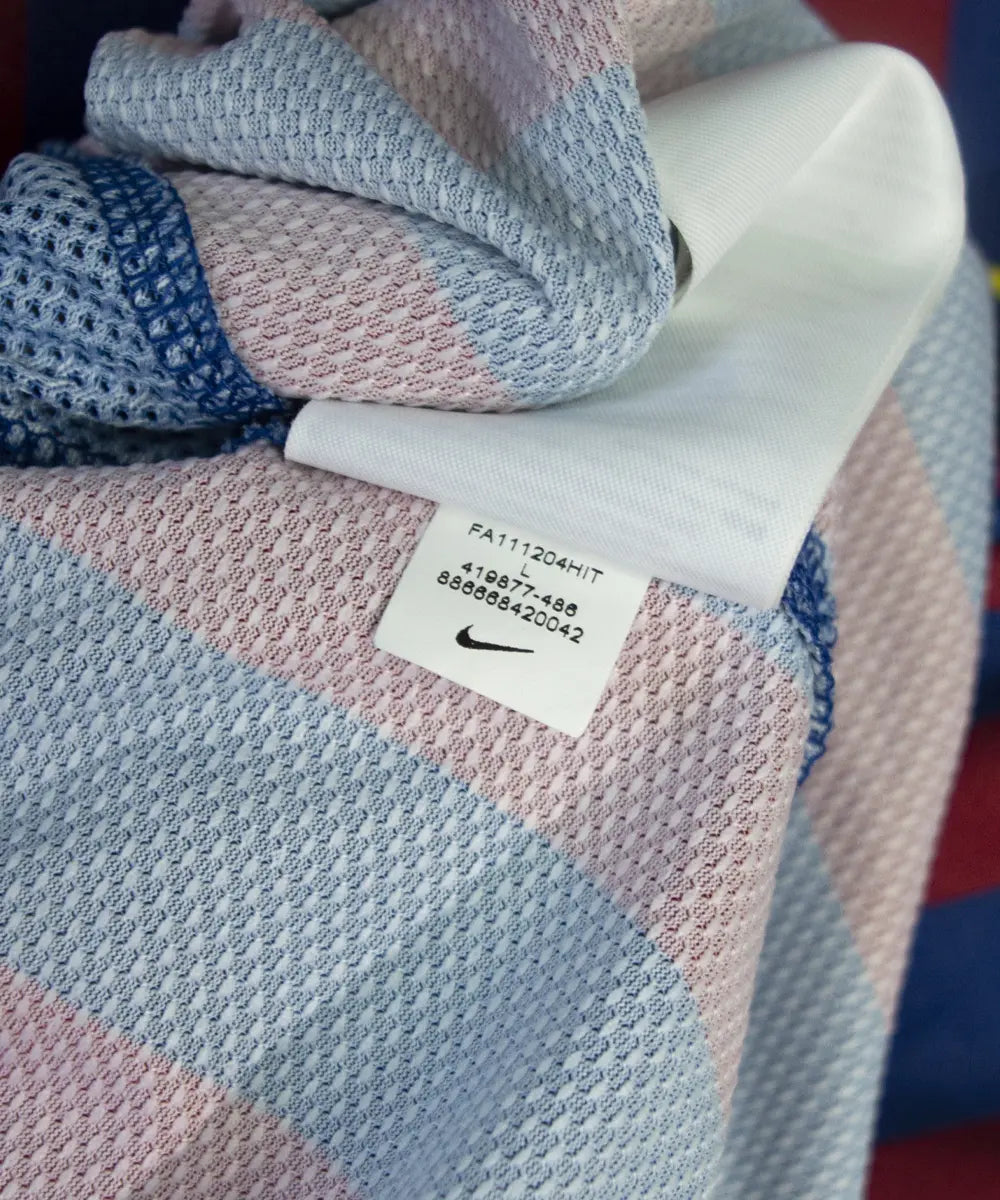 Maillot domicile bleu et rouge du fc barcelone de la saison 2011-2012. On peut retrouver le sponsor qatar foundation, le sponsor unicef et l'équipementier nike. Le maillot est floqué du numéro 10 Leo Messi. Sur cette photo on peut voir l"étiquette d'authenticité comportant les numéros 419877-486