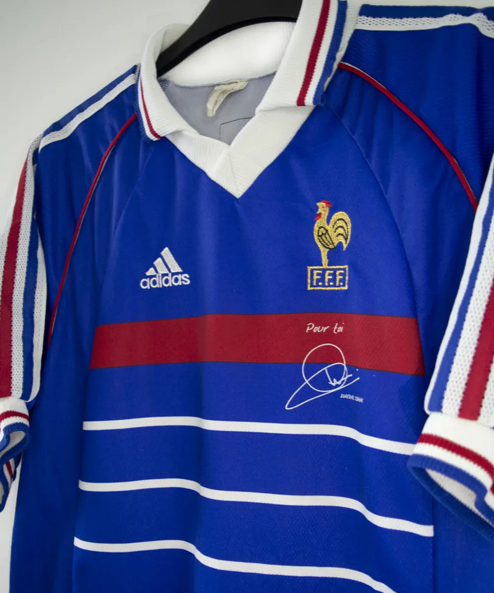 Maillot de foot vintage domicile bleu blanc et rouge de l'équipe de france 1998. On peut retrouver l'équipementier adidas. Le maillot possède la signature pour toi zinedine zidane. Il s'agit d'un maillot authentique