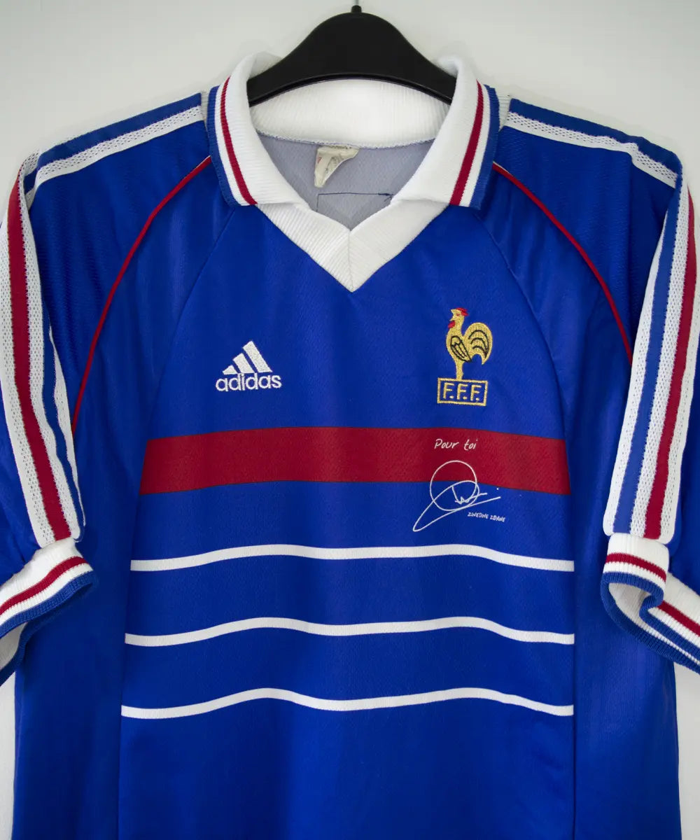 Maillot de foot vintage domicile bleu blanc et rouge de l'équipe de france 1998. On peut retrouver l'équipementier adidas. Le maillot possède la signature pour toi zinedine zidane. Il s'agit d'un maillot authentique
