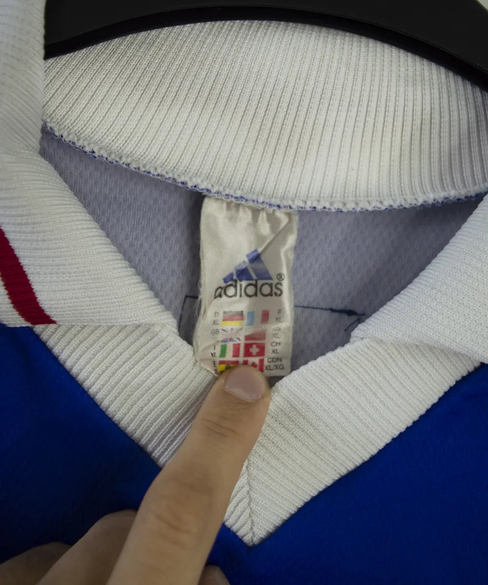 Maillot de foot vintage domicile bleu blanc et rouge de l'équipe de france 1998. On peut retrouver l'équipementier adidas. Le maillot possède la signature pour toi zinedine zidane. Il s'agit d'un maillot authentique