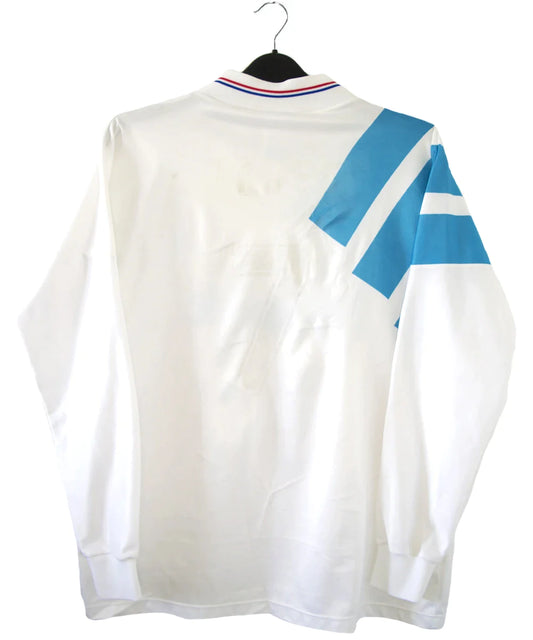 Maillot de foot vintage domicile blanc et bleu de l'OM de la saison 1991/1992. On peut retrouver l'équipementier adidas et le sponsor Panasonic. Le maillot est signé par plusieurs joueurs de l'époque dont Didier Deschamps et Jean Pierre Papin. Il s'agit d'un maillot authentique.