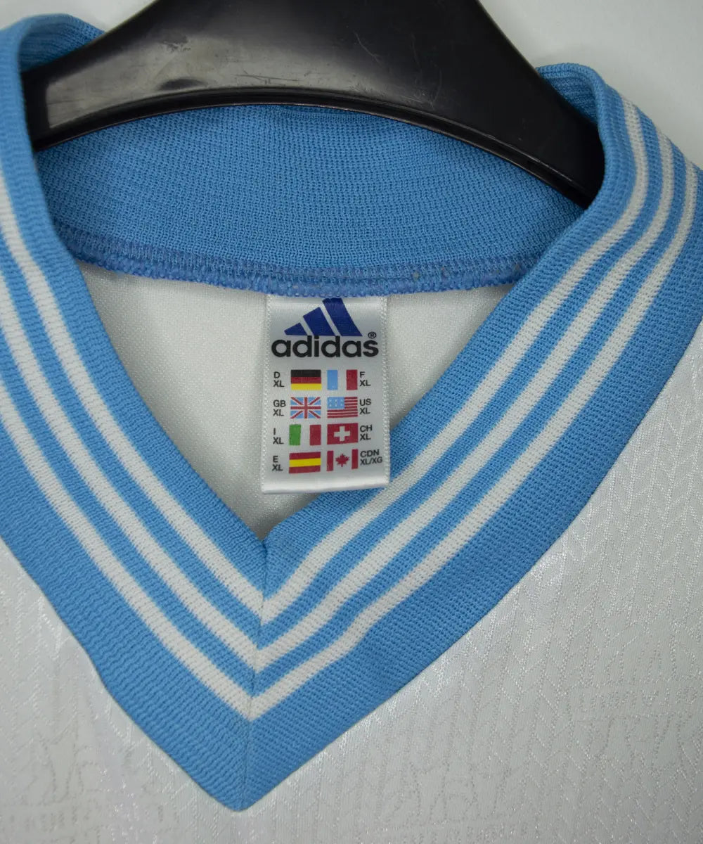 Maillot vintage domicile banc et bleu de l'OM de la saison 1997-1998. On peut retrouver l'équipementier adidas et le sponsor ericsson