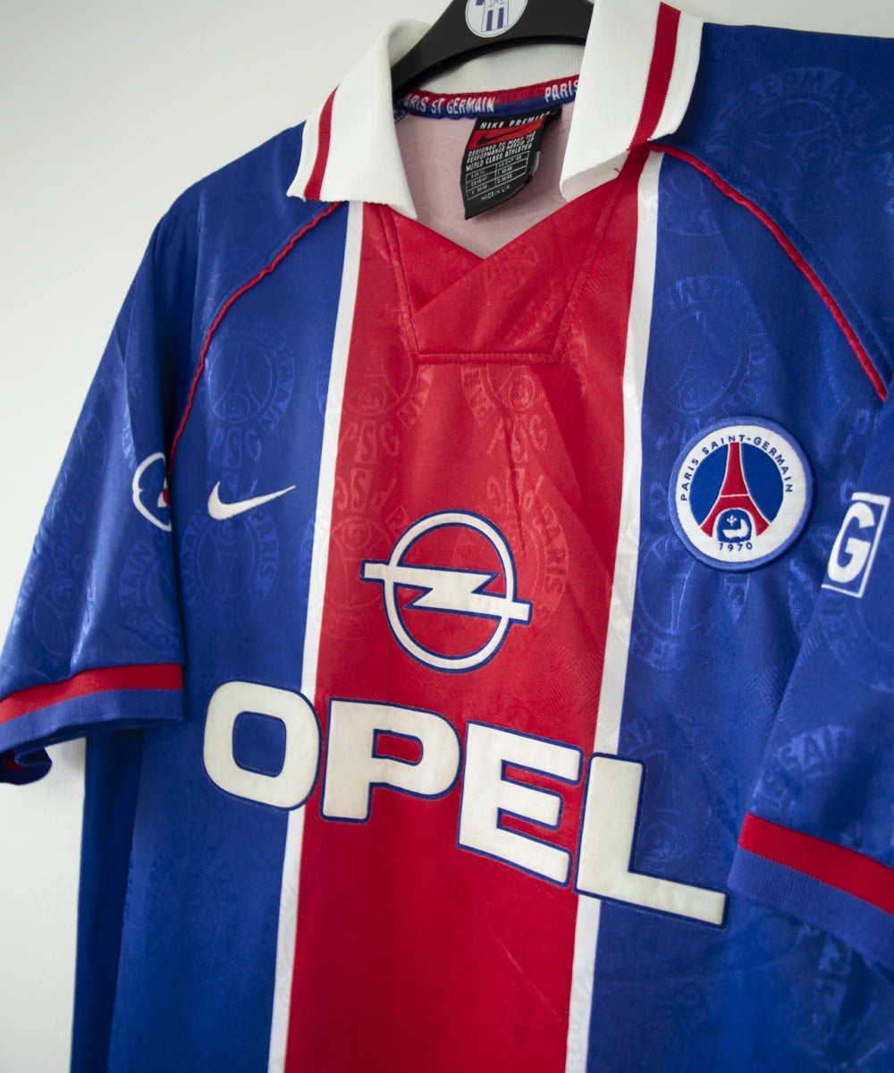 Maillot de foot vintage bleu blanc et rouge du psg de la saison 1996/1997. On peut retrouver l'équipementier nike et le sponsor opel. Il s'agit d'un maillot authentique d'époque