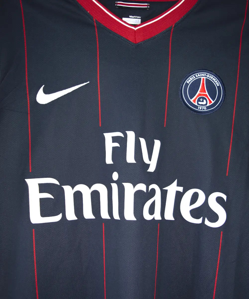 Maillot domicile du psg de la saison 2009 2010. Le maillot est de couleur bleu avec des rayures rouges. On peut retrouver l'équipementier nike, le sponsor fly emirates et le sponsor poweo. Le maillot est floqué ludovic Giuly. Sur cette photo on peut voir le devant du maillot de près