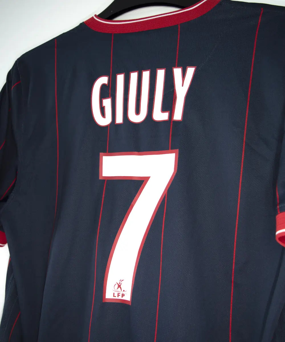 Maillot domicile du psg de la saison 2009 2010. Le maillot est de couleur bleu avec des rayures rouges. On peut retrouver l'équipementier nike, le sponsor fly emirates et le sponsor poweo. Le maillot est floqué ludovic Giuly. Sur cette photo on peut voir le flocage de côté
