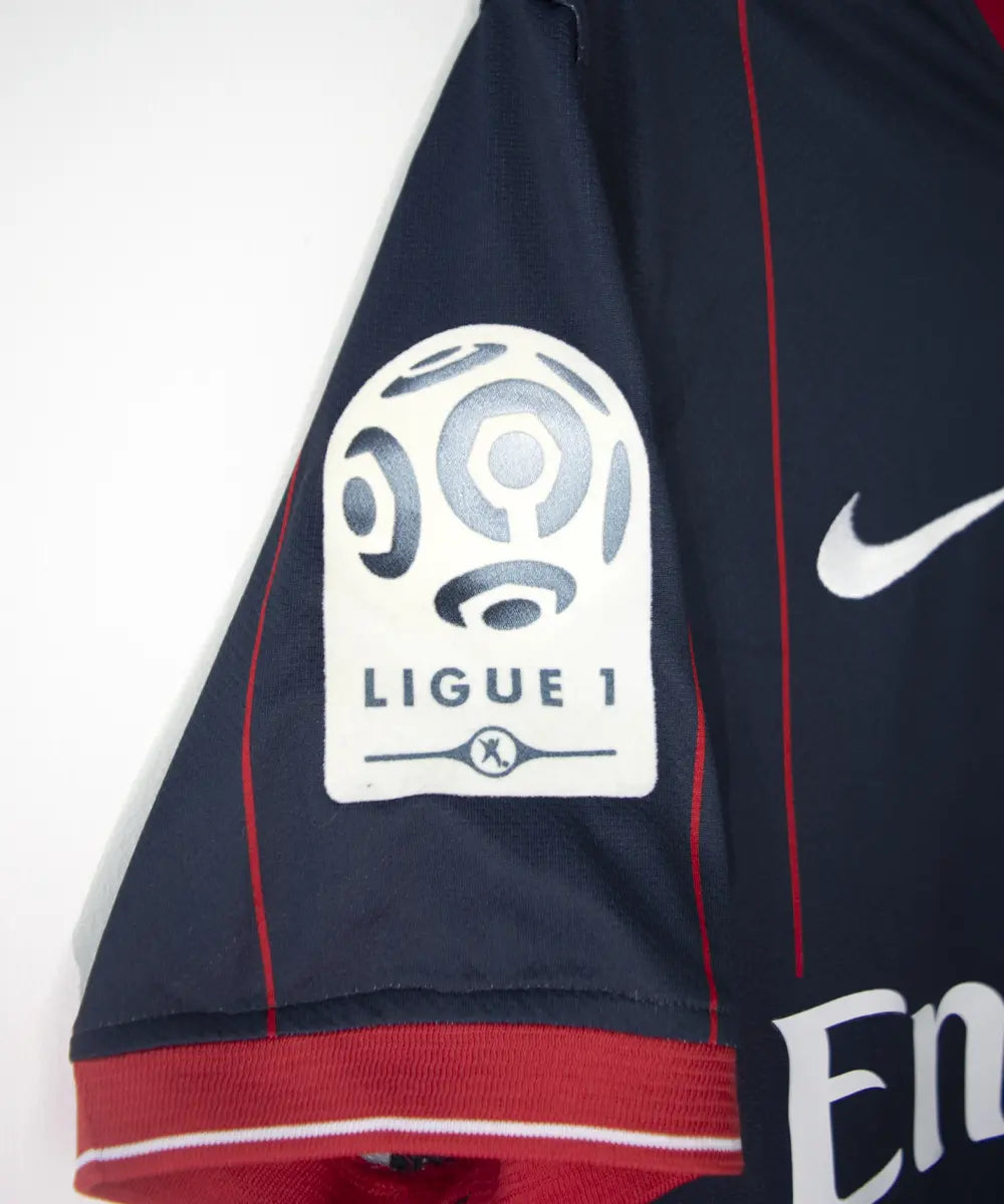 Maillot domicile du psg de la saison 2009 2010. Le maillot est de couleur bleu avec des rayures rouges. On peut retrouver l'équipementier nike, le sponsor fly emirates et le sponsor poweo. Le maillot est floqué ludovic Giuly. Sur cette photo on peut voir le patch de la ligue 1