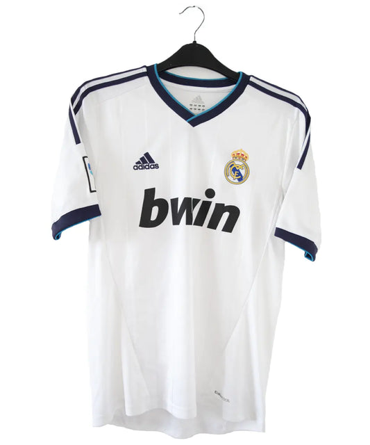 Maillot blanc et bleu du real madrid de la saison 2012-2013. On peut retrouver sur le maillot le sponsor bwin et l'équipementier adidas. Le maillot porte aussi le patch des 110 ans du real et le patch de la LFP.