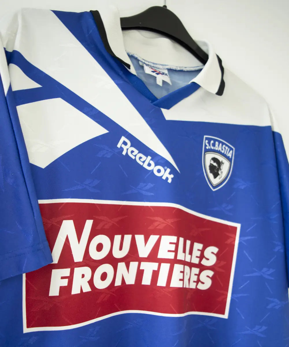 Maillot domicile bleu et blanc du sc bastia de la saison 1995-1997. On peut retrouver l'équipementier reebok, et le sponsor nouvelles frontières. Sur cette photo on peut voir le maillot de côté