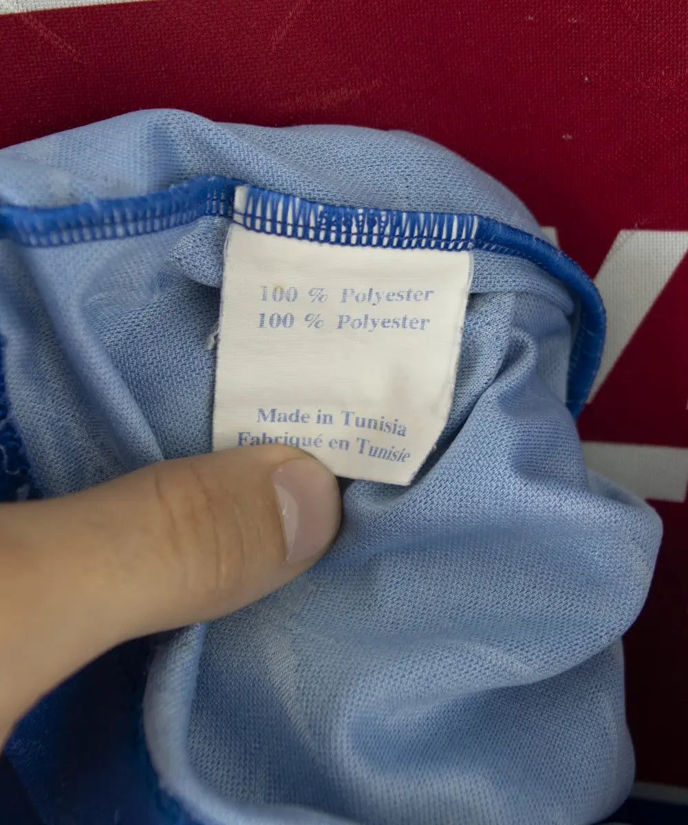 Maillot domicile bleu et blanc du sc bastia de la saison 1995-1997. On peut retrouver l'équipementier reebok, et le sponsor nouvelles frontières. Sur cette photo on peut voir l'étiquette d'authenticité du maillot