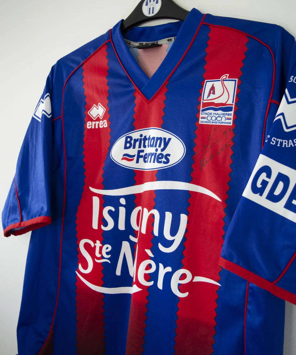 Maillot de foot vintage domicile du Stade Malherbe Caen édité lors de la finale de la Coupe de la Ligue lors de la saison 2004-2005. On peut retrouver l'équipementier Errea, le sponsor isigny Ste Mère, Brittany Ferries, Phillips et GDE. Le maillot est signé par Ibrahima Faye. Il s'agit d'un maillot authentique