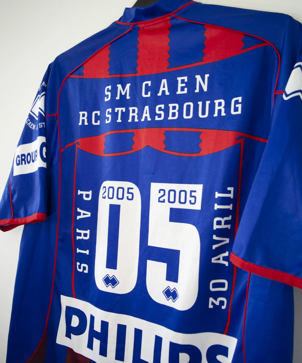 Maillot de foot vintage domicile du Stade Malherbe Caen édité lors de la finale de la Coupe de la Ligue lors de la saison 2004-2005. On peut retrouver l'équipementier Errea, le sponsor isigny Ste Mère, Brittany Ferries, Phillips et GDE. Le maillot est signé par Ibrahima Faye. Il s'agit d'un maillot authentique