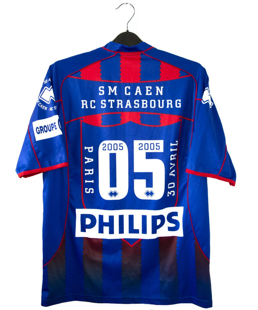 Maillot de foot vintage domicile du Stade Malherbe Caen édité lors de la finale de la Coupe de la Ligue lors de la saison 2004-2005. On peut retrouver l'équipementier Errea, le sponsor isigny Ste Mère, Brittany Ferries, Phillips et GDE. Le maillot est signé par Ibrahima Faye. Il s'agit d'un maillot authentique