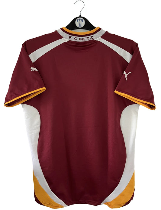 Maillot de foot vintage domicile rouge blanc et jaune du FC Metz de la saison 2001/2002. On peut retrouver l'équipementier Puma et le sponsor Sollac. Il s'agit d'un maillot authentique d'époque.