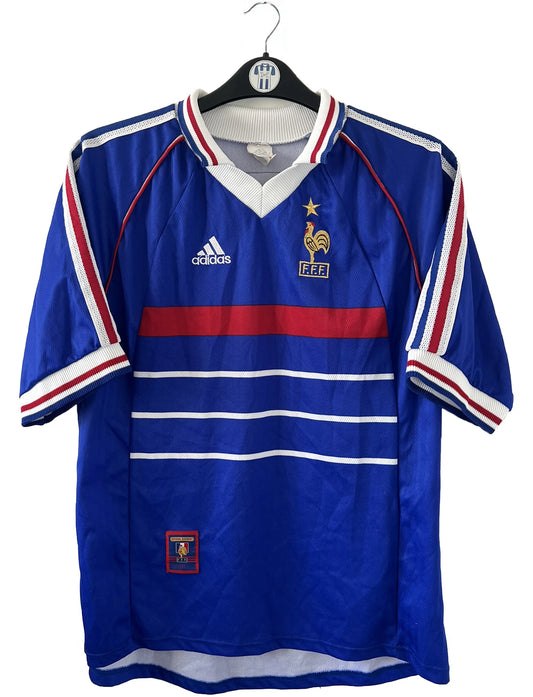 Maillot de foot vintage domicile bleu de l'équipe de france 1998. On peut retrouver l'équipementier Adidas. Le maillot est floqué du numéro 10 Zinedine Zidane. Il s'agit d'un maillot authentique d'époque.