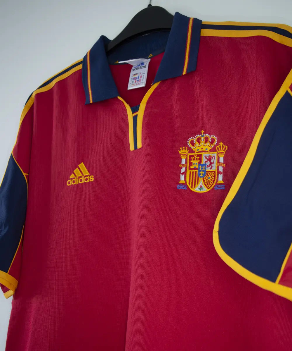 Maillot domicile de l'espagne de couleur rouge, bleu et jaune de 1999 à 2002. On peut retrouver l'équipementier adidas.