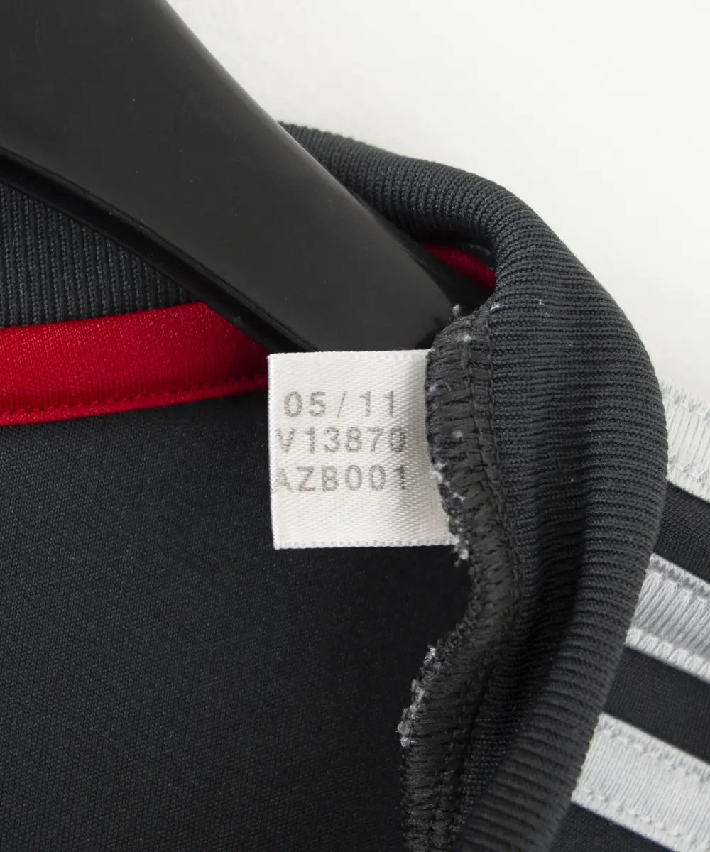 Maillot extérieur de liverpool de la saison 2011-2012. Le maillot est de couleur noir, gris et rouge. On peut retrouver l'équipementier adidas et le sponsor standard chartered. Sur cette photo on peut voir l'étiquette comportant les numéros V13870