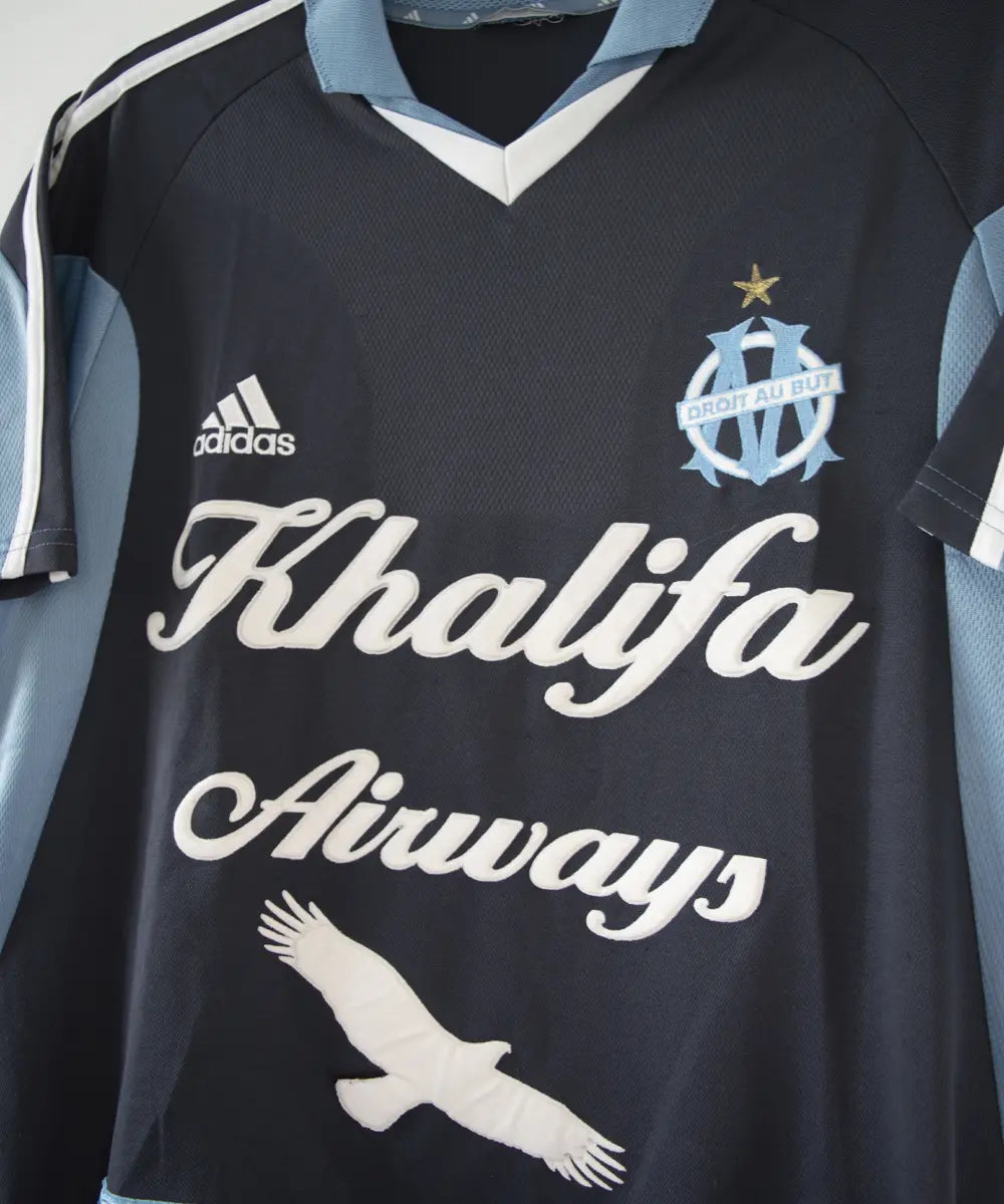 Maillot extérieur de l'OM de couleur bleu, blanc et noir. On peut retrouver l'équipementier adidas et le sponsor khalifa airways