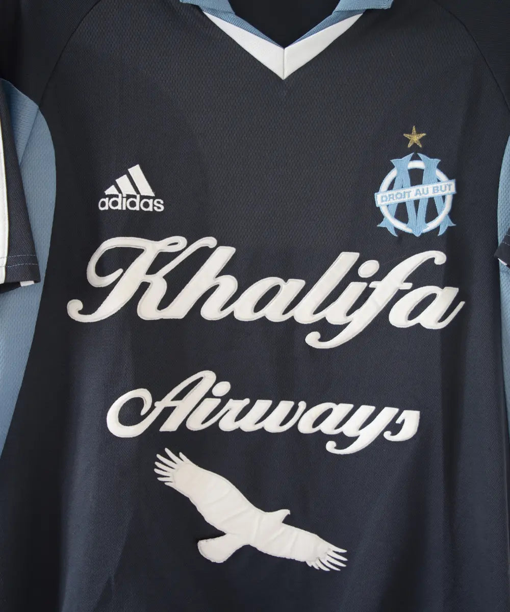 Maillot extérieur de l'OM de couleur bleu, blanc et noir. On peut retrouver l'équipementier adidas et le sponsor khalifa airways