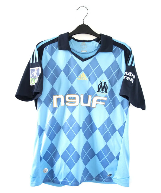 Maillot extérieur de face bleu clair et bleu foncé de l'om de la saison 2008-2009. Le maillot est floqué du numéro 20 Ben Arfa. On peut retrouver sur le maillot, l'équipementier adidas, le sponsor neuf, le sponsor nasuba et le sponsor groupama