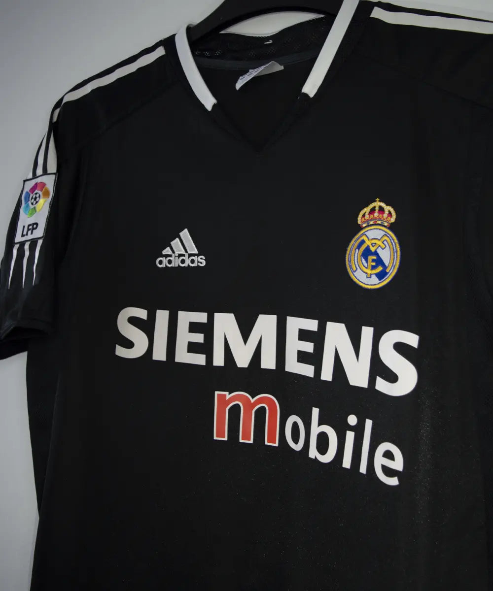 Maillot vintage extérieur noir et blanc du real madrid de la saison 2004-2005. On peut retrouver l'équipementier adidas et le sponsor siemens mobile. Le maillot est floqué du numéro 5 Zinedine Zidane