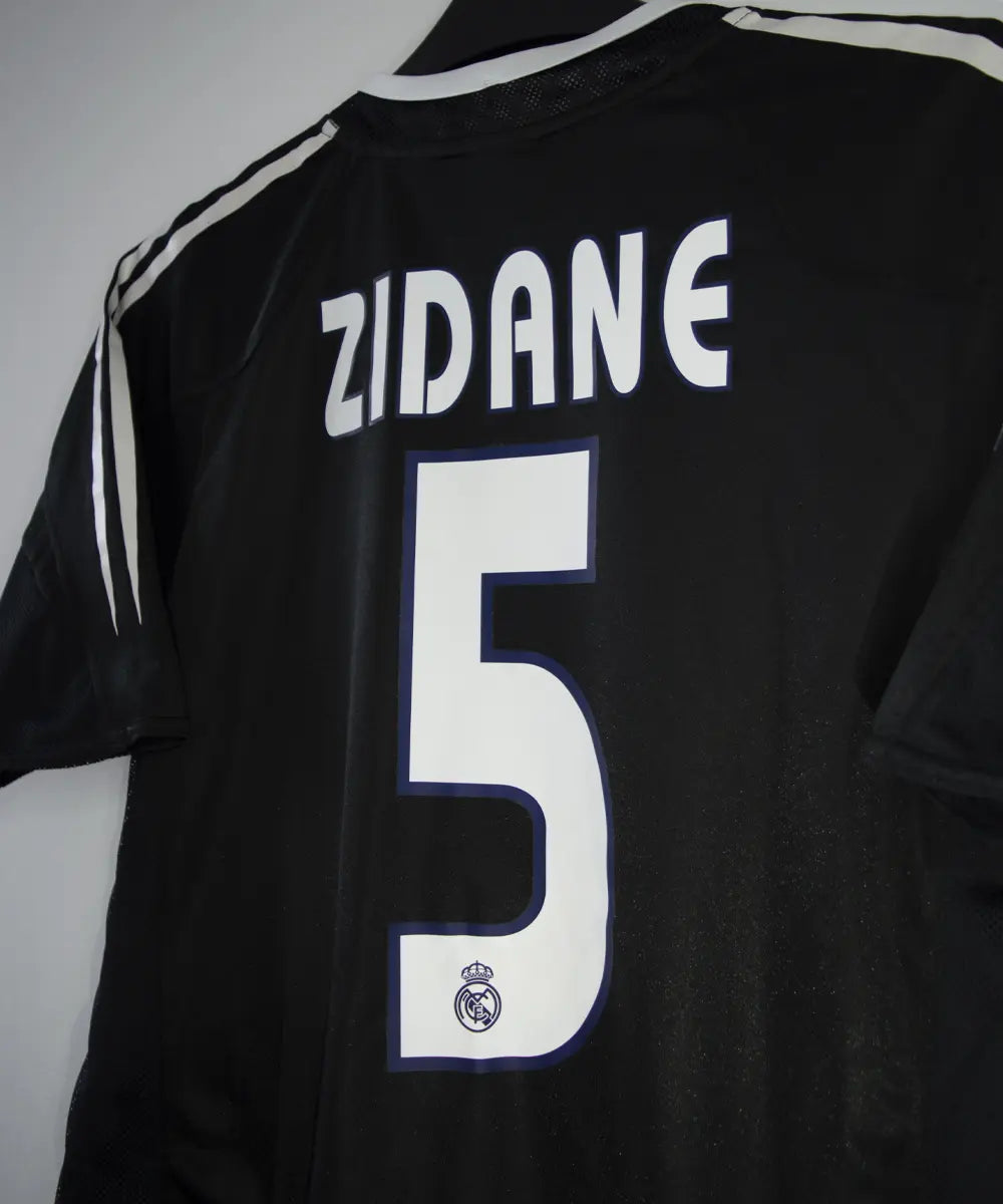 Maillot vintage extérieur noir et blanc du real madrid de la saison 2004-2005. On peut retrouver l'équipementier adidas et le sponsor siemens mobile. Le maillot est floqué du numéro 5 Zinedine Zidane
