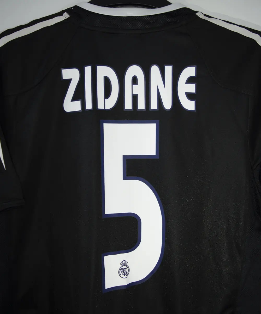 Maillot vintage extérieur noir et blanc du real madrid de la saison 2004-2005. On peut retrouver l'équipementier adidas et le sponsor siemens mobile. Le maillot est floqué du numéro 5 Zinedine Zidane