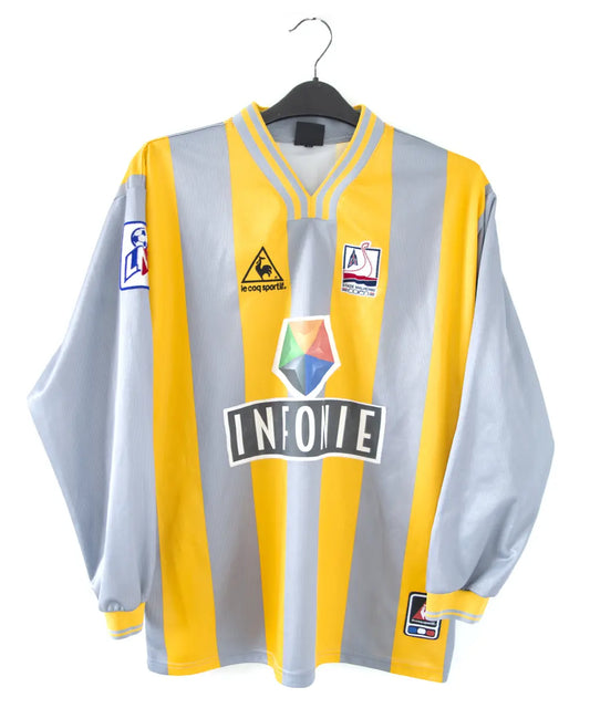 Maillot du SM Caen de la saison 2000-2001. Le maillot est de couleur gris et jaune. On peut retrouver l'équipementier le coq sportif, le sponsor infonie et le sponsor isigny sainte mère. On peut aussi retrouver l'ancien patch LNF. Le maillot est floqué du numéro 20 Faderne
