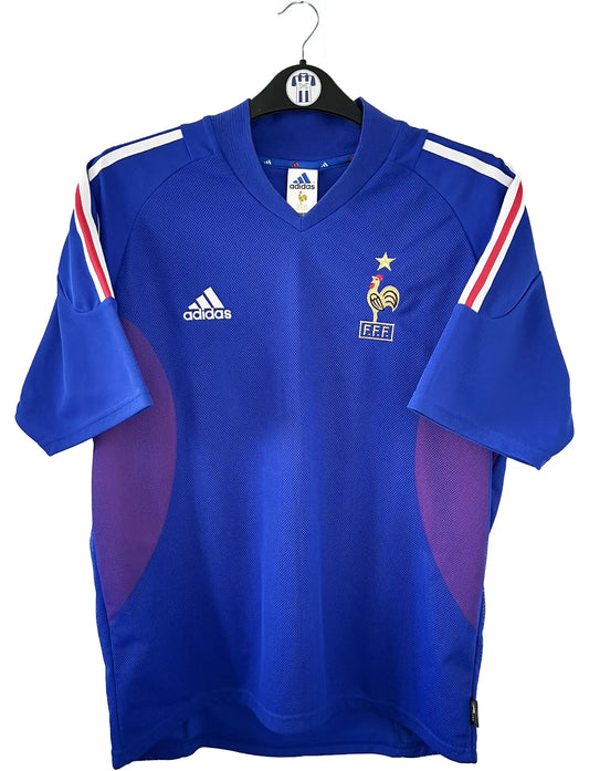 Maillot de foot vintage domicile de l'équipe de france 2002. Le maillot est de couleur bleu blanc et rouge. On peut retrouver l'équipementier adidas. Le maillot est floqué du numéro 10 Zinedine Zidane. Il s'agit d'un maillot authentique d'époque comportant les numéros 139531.