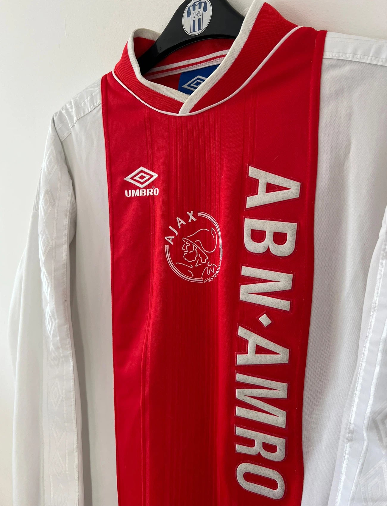 Maillot de foot vintage domicile rouge et blanc de l'Ajax Amsterdam saison 1999/2000. On peut retrouver l'équipementier Umbro et le sponsor ABN-AMRO. Il s'agit d'un maillot authentique d'époque issu du stock pro.