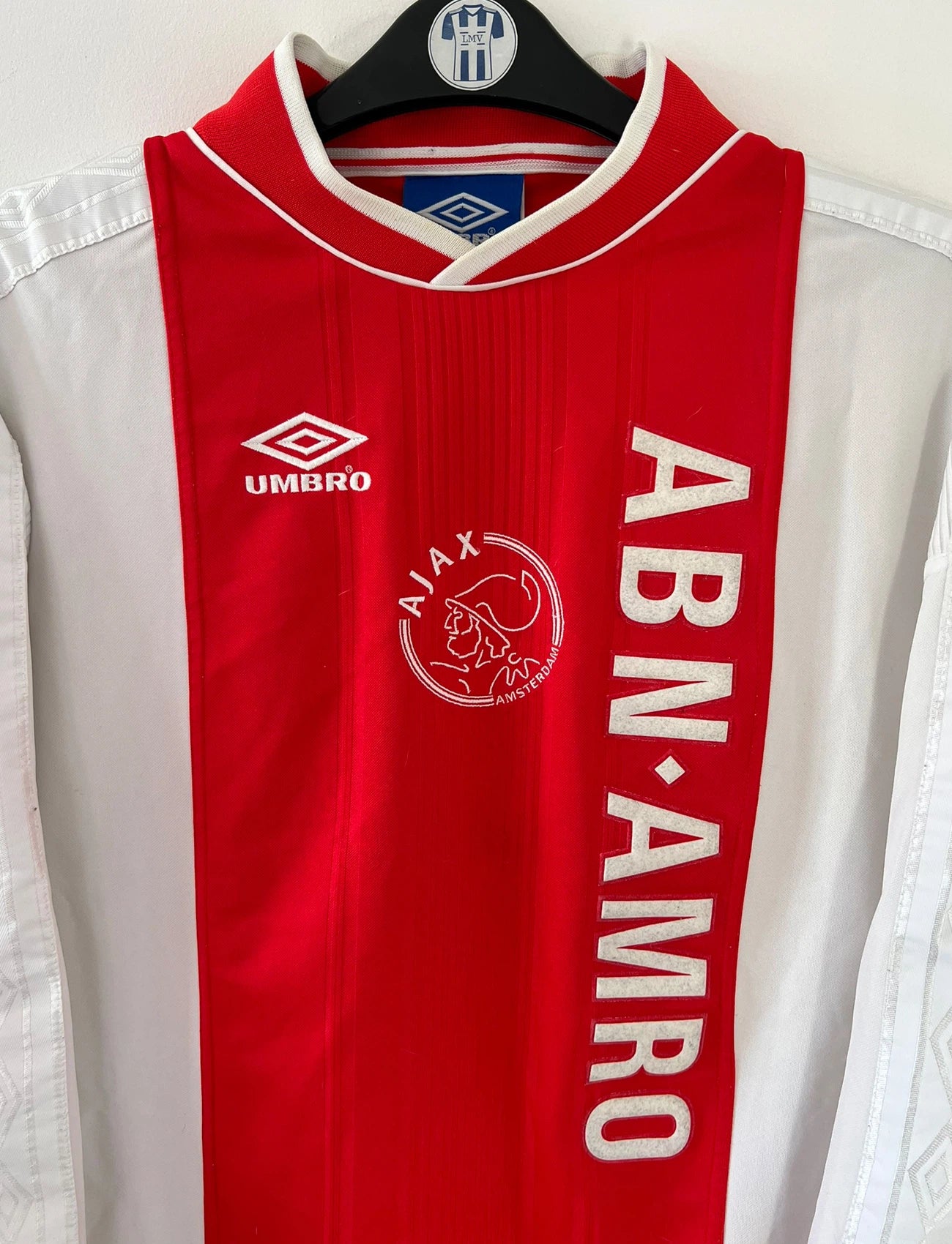 Maillot de foot vintage domicile rouge et blanc de l'Ajax Amsterdam saison 1999/2000. On peut retrouver l'équipementier Umbro et le sponsor ABN-AMRO. Il s'agit d'un maillot authentique d'époque issu du stock pro.