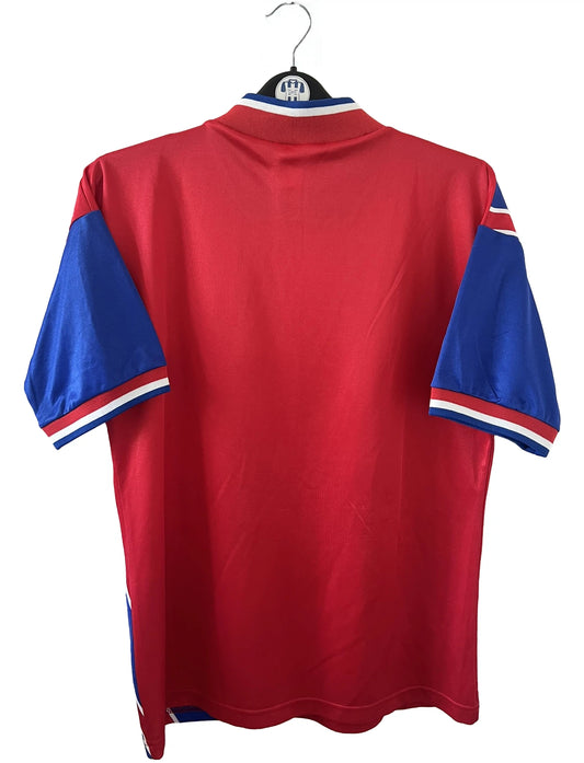 Maillot de foot vintage domicile rouge et bleu du Bayern de la saison 1993/1995. On peut retrouver l'équipementier Adidas et le sponsor Opel. Il s'agit d'un maillot authentique d'époque.