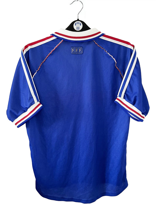 Maillot de foot vintage bleu, blanc et rouge de l'équipe de france 1998. On peut retrouver l'équipementier adidas. Il s'agit d'un maillot authentique édité avant la finale de la coupe du monde car celui-ci ne possède pas l'étoile. Le maillot possède la mention pour toi avec la signature de zidane