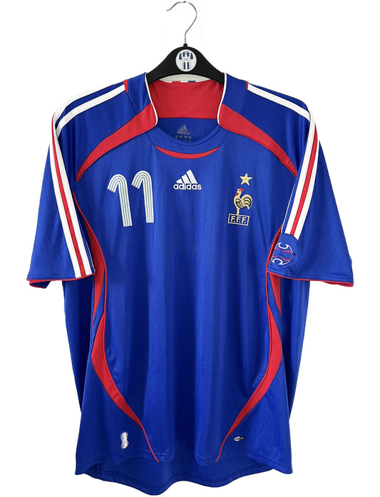 Maillot de foot vintage domicile bleu, blanc et rouge de l'équipe de france 2006. On peut retrouver l'équipementier adidas. Le maillot est floqué du numéro 11 Sylvain Wiltord. Il s'agit d'un maillot authentique d'époque comportant l'étiquette 740126